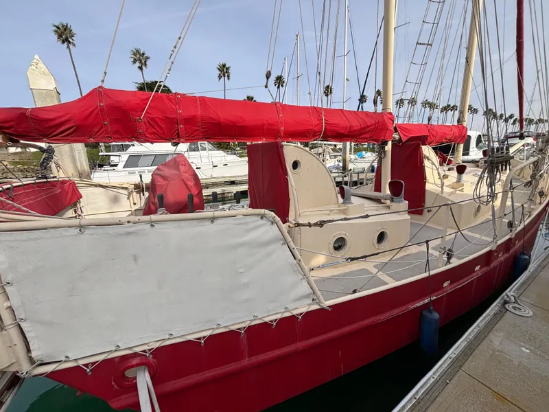 1975 Custom 45’ Thomas Colvin “Tamarack” Schooner with red sails docked at marina.