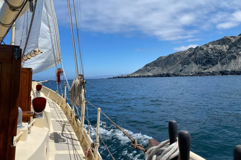 Sailing on a 1975 Custom 45’ Thomas Colvin “Tamarack” Schooner near rocky coastline.