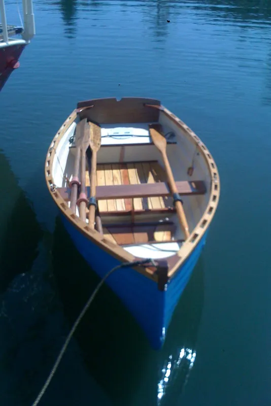 Blue wooden rowboat on calm water, part of 1975 Custom 45’ Thomas Colvin “Tamarack” Schooner.