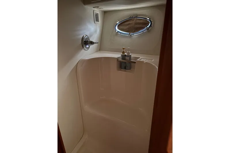 Shower area inside 2000 Silverton 42 Convertible yacht with porthole and toiletries.