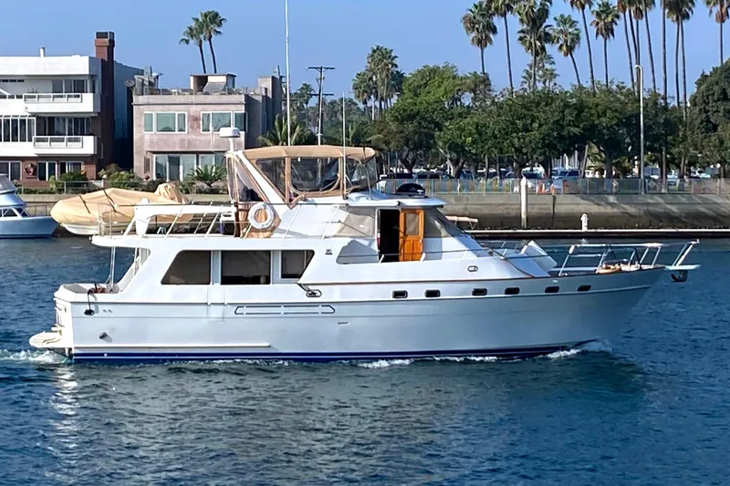1987 MedYacht Mallorca 50 cruising near waterfront homes and palm trees.