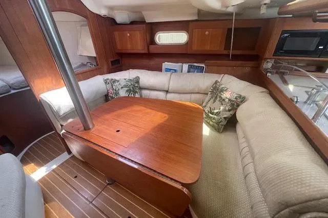 Cozy interior of 2001 Hunter 380 sailboat with wooden table and cushioned seating.