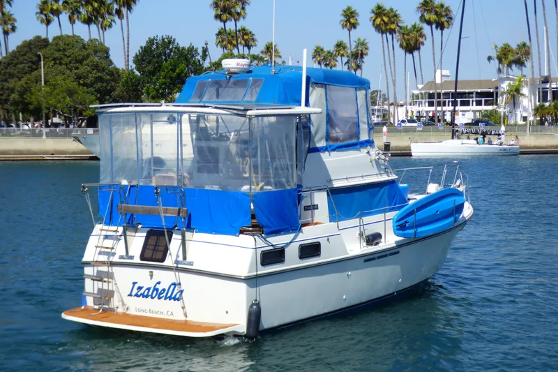 1985 Carver 3607 Aft Cabin Motor Yacht in marina, blue canopy, palm trees in background.