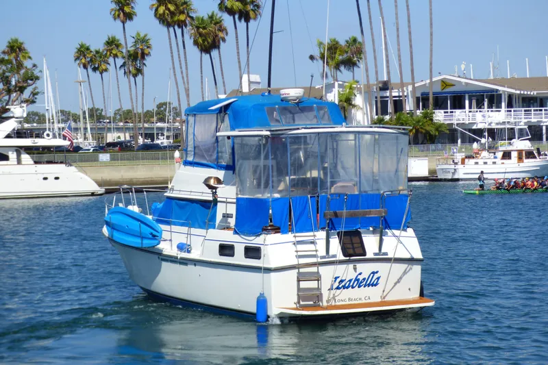 1985 Carver 3607 Aft Cabin Motor Yacht in marina, blue canopy, palm trees in background.