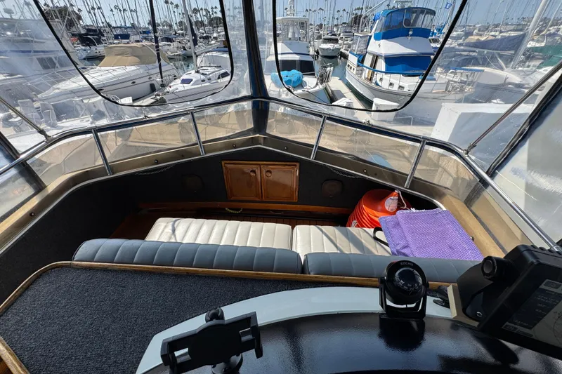 1985 Carver 3607 Aft Cabin Motor Yacht helm with marina view, featuring seating and navigation equipment.