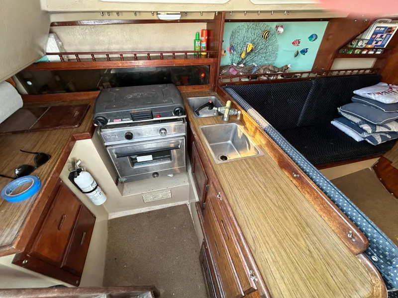 Interior of a 1981 Catalina 30 sailboat kitchen with stove, sink, and seating area.