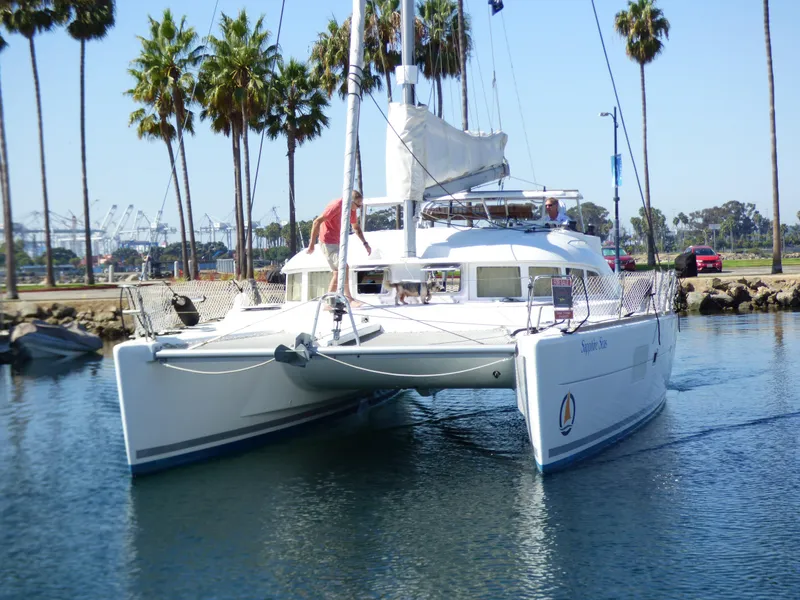 2015 Lagoon 380 catamaran sailing near palm trees in a marina.