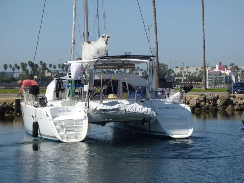 2015 Lagoon 380 catamaran sailing in a marina with palm trees in the background.