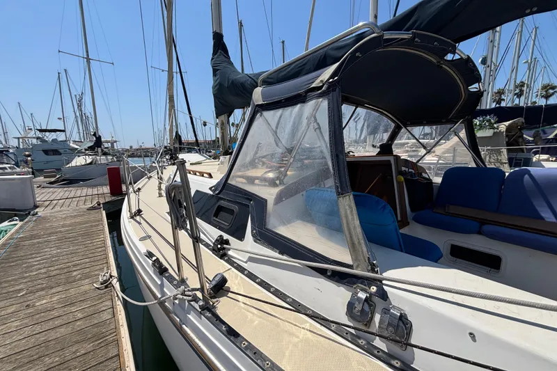 1987 Catalina 34 sailboat docked at marina, featuring blue seating and protective canopy.