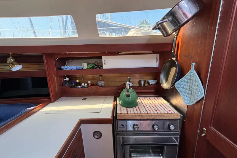 Cozy 1987 Catalina 34 yacht kitchen with stove, kettle, and hanging cookware.