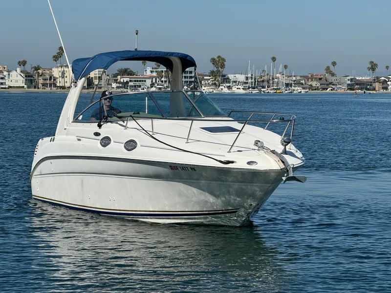 2003 Sea Ray 260 Sundancer boat cruising on calm waters near a marina.