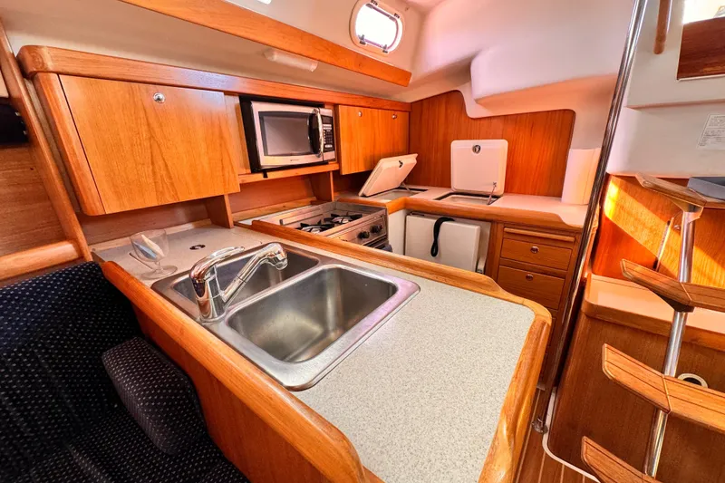 2004 Catalina 350 yacht kitchen with sink, stove, microwave, and wooden cabinetry.
