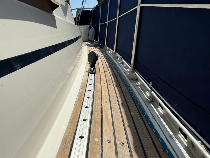 Side deck of 1985 Nauticat 43 sailboat with wooden planks and metal railing.