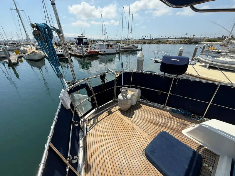 Deck of 1985 Nauticat 43 sailboat in marina, featuring wooden flooring and moored boats.