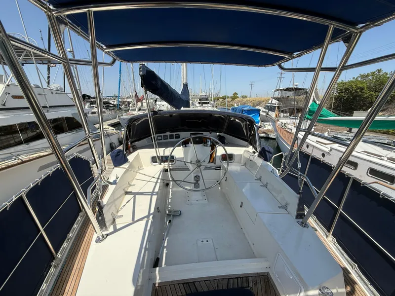 1985 Nauticat 43 sailboat cockpit with steering wheel, docked in marina under blue canopy.