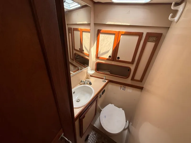 Bathroom interior of 1985 Nauticat 43 yacht, featuring sink, toilet, and wooden cabinetry.