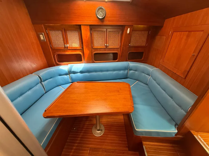 Interior of 1985 Nauticat 43 sailboat with blue cushioned seating and wooden table.