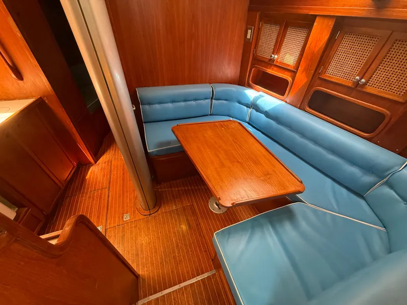 Interior of 1985 Nauticat 43 yacht with blue seating and wooden table.