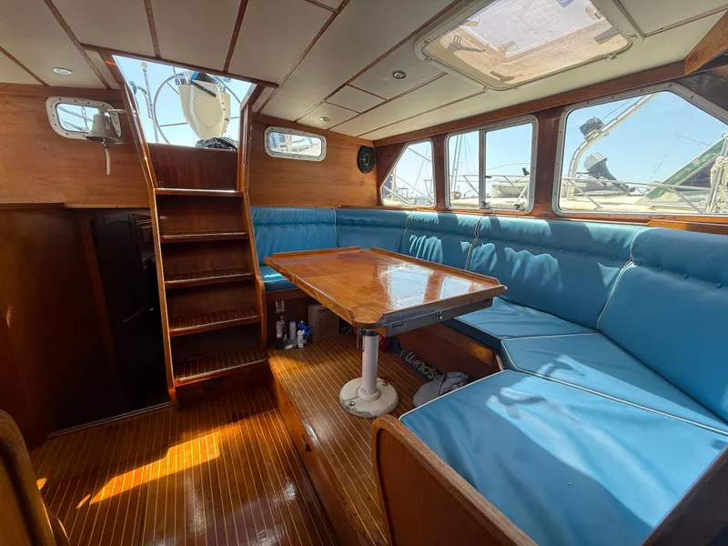 Interior of 1985 Nauticat 43 sailboat with blue cushioned seating and wooden table.