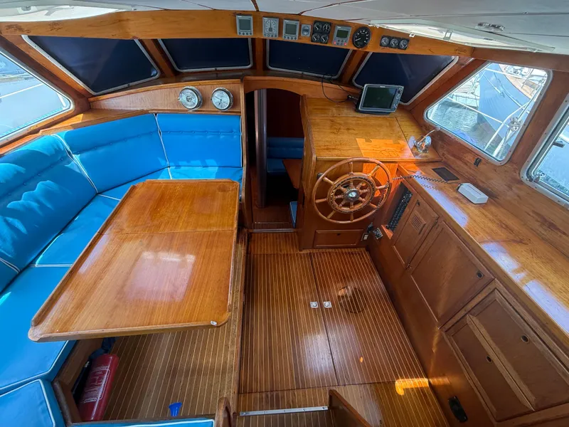 Interior of 1985 Nauticat 43 sailboat with wooden helm, blue seating, and navigation instruments.