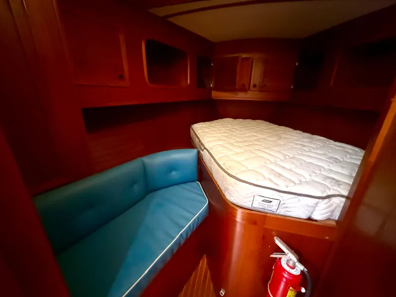 Cozy cabin interior of 1985 Nauticat 43 with bed, blue seating, and fire extinguisher.