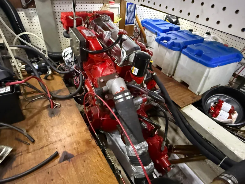 Engine room of a 1985 Nauticat 43 sailboat with red engine and storage containers.