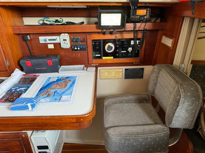 Navigation station inside 1989 Catalina Sloop, featuring control panel, chair, and nautical charts.