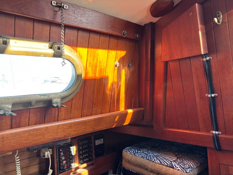 Interior of a 1977 Baba 30 sailboat with wooden paneling and a porthole window.