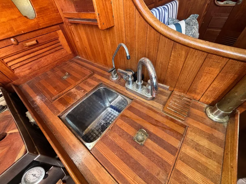 Wooden interior of a 1977 Baba 30 sailboat with a compact kitchen sink.