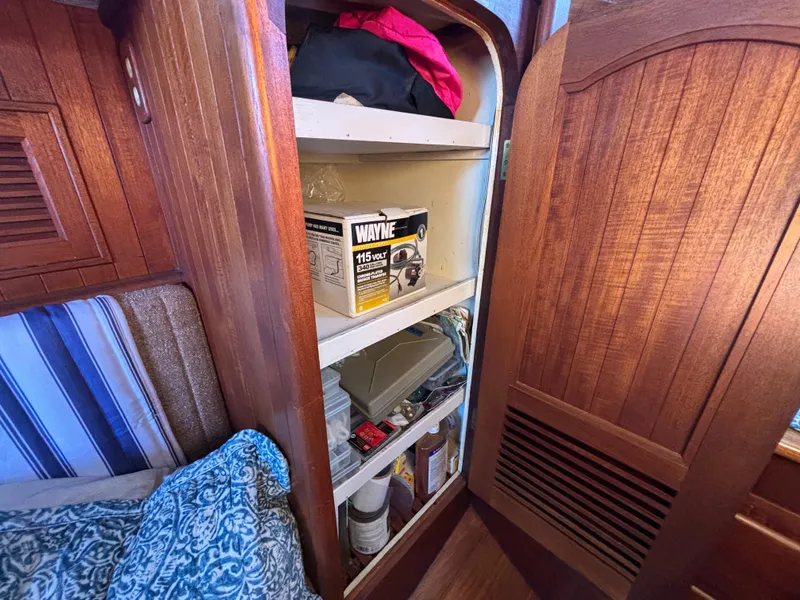 Wooden cabinet with shelves inside a 1977 Baba 30 boat, storing various items.