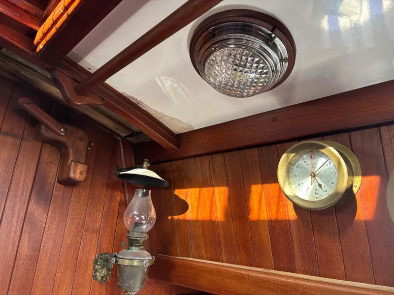 Interior of a 1977 Baba 30 sailboat with wooden paneling, vintage lamp, and brass barometer.