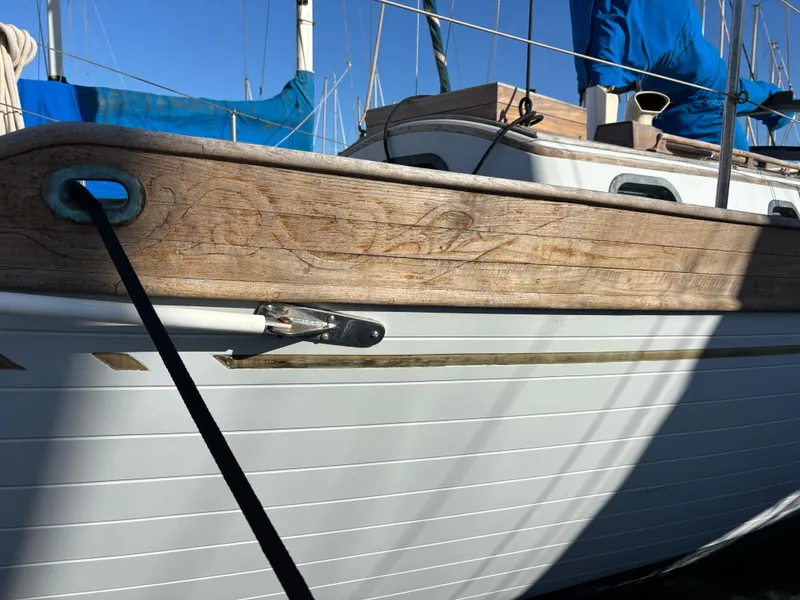 1977 Baba 30 sailboat with wooden detailing and blue sails in a marina.