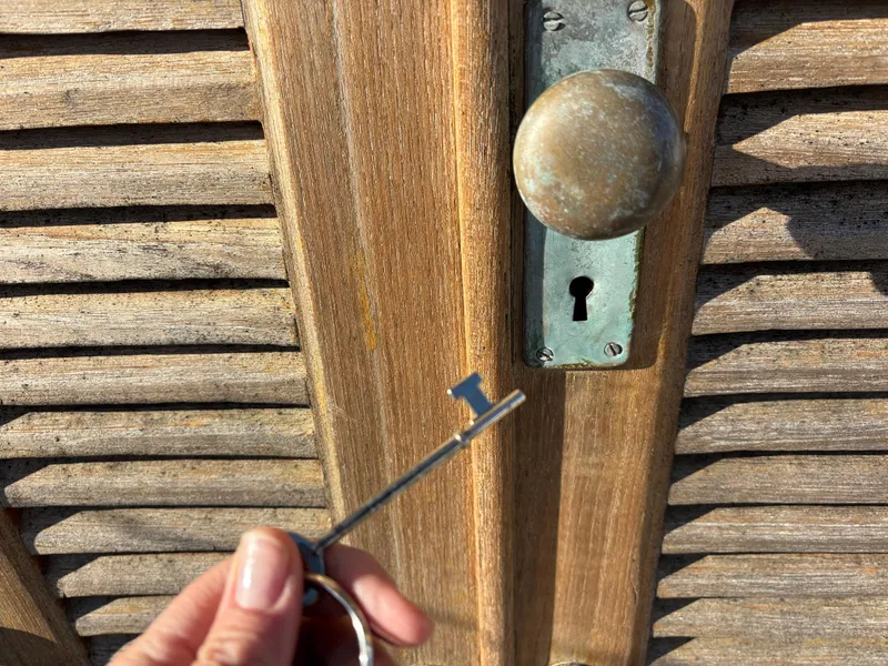 Hand holding key near vintage wooden door with round knob and keyhole, Baba 30, 1977.