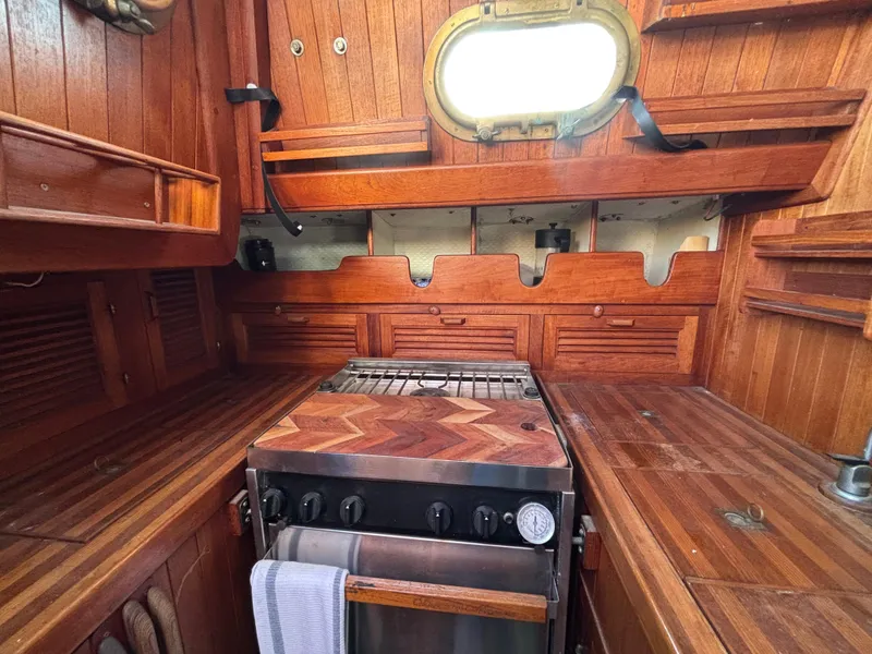 1977 Baba 30 yacht galley with wooden cabinetry and stove, featuring a porthole window.
