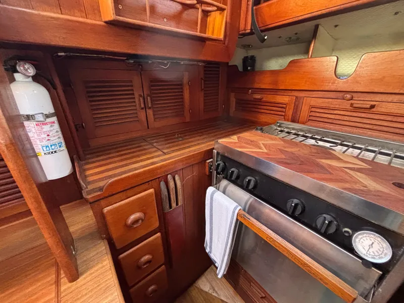 Wooden interior of a 1977 Baba 30 sailboat galley with stove and storage cabinets.