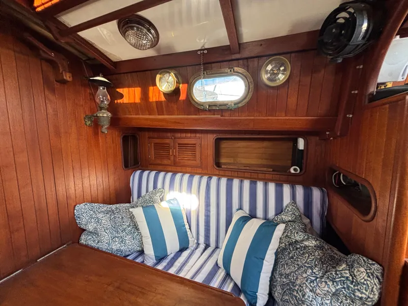 Cozy 1977 Baba 30 sailboat interior with striped cushions and wooden paneling.