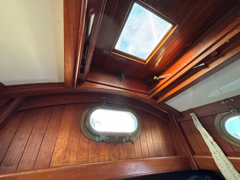 Interior of a 1977 Baba 30 sailboat, featuring wooden paneling and porthole windows.