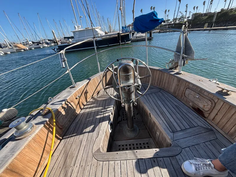 1977 Baba 30 sailboat cockpit with wooden deck, steering wheel, and marina view.