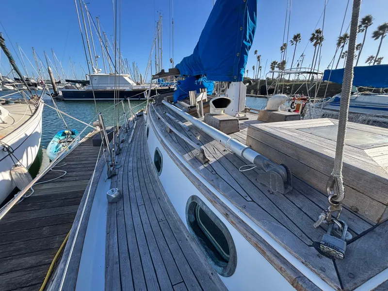 Sailboat docked at marina, Baba 30 model, 1977, with wooden deck and blue sail cover.