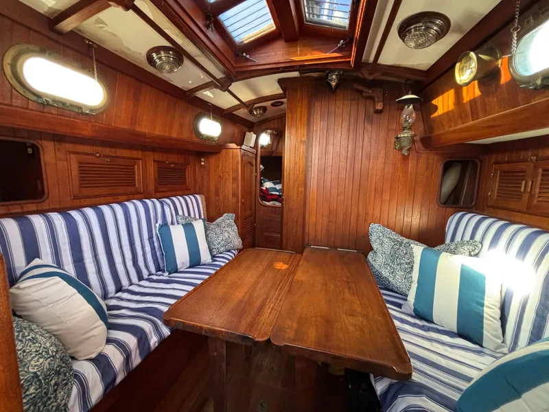 Cozy 1977 Baba 30 sailboat interior with striped cushions and wooden paneling.
