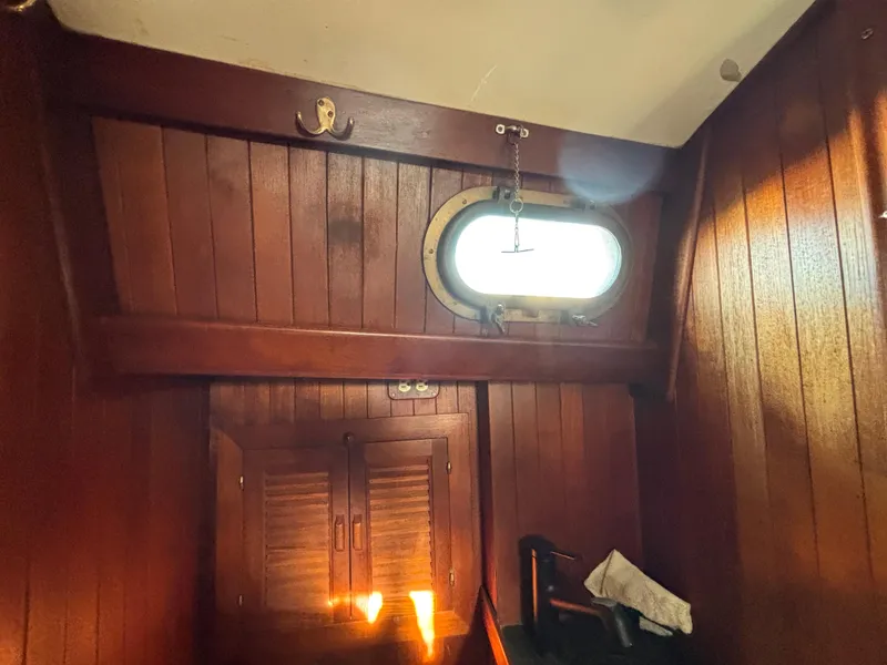 Interior of a 1977 Baba 30 sailboat with wooden paneling and a porthole window.