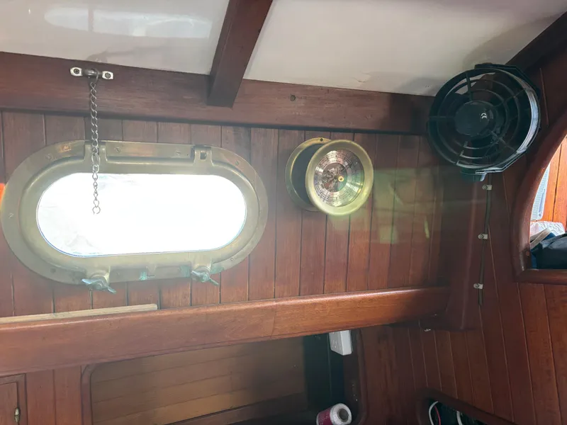 Interior of a 1977 Baba 30 sailboat with wooden paneling, porthole, and fan.