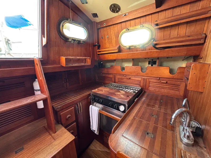 1977 Baba 30 sailboat interior with wooden cabinetry, stove, and portholes.