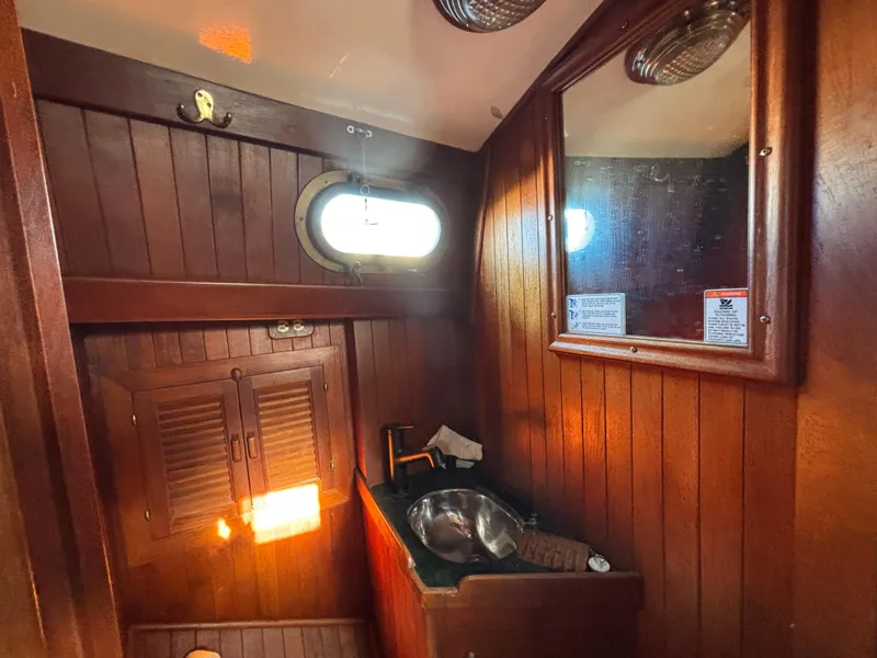 Wood-paneled bathroom interior of a 1977 Baba 30 sailboat with sink and porthole window.