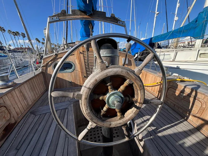 Wooden steering wheel on a 1977 Baba 30 sailboat, docked in a marina.