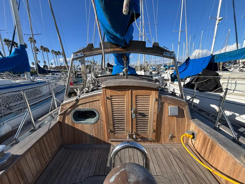 1977 Baba 30 sailboat with wooden deck and blue sails in a marina.