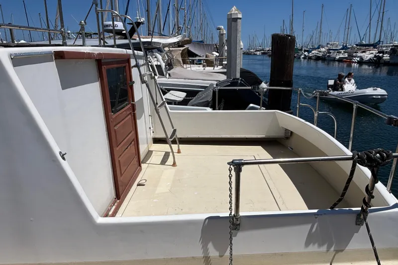1974 Skookum 34 boat docked at marina, featuring open deck and wooden door.