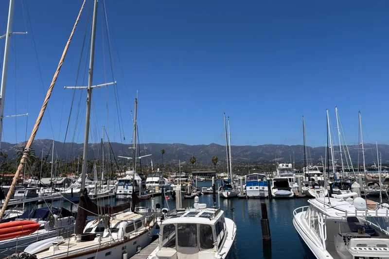 Boats docked at a marina with mountains in the background under a clear blue sky.