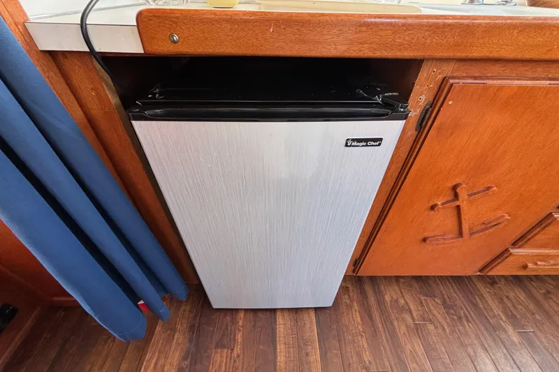 Compact Magic Chef fridge in a 1974 Skookum 34 boat kitchen, with wooden cabinetry.