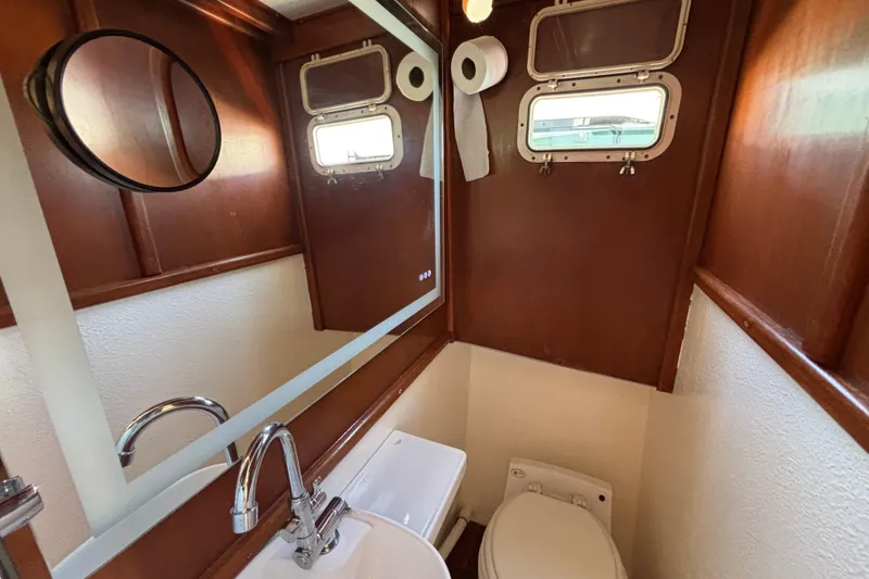 Compact bathroom in a 1974 Skookum 34 boat, featuring wood paneling and nautical windows.